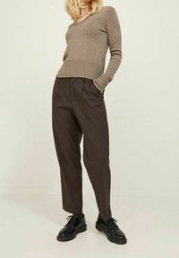 Bruna, skräddarsydda byxor med veck, kombinerade med en figurnära, ljusbrun V-ringad tröja. Svarta snörskor fulländar outfiten.