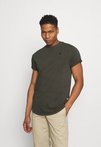 Camiseta de color verde oliva oscuro, de mangas cortas, cuello redondo, con el dobladillo ligeramente curvado, pequeño logo en el pecho, fabricada con material de algodón suave.