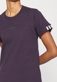 Lila bomull t-shirt med kort ärm, med rundad halsringning, ton-i-ton sömmar och vita ränder på ärmen. Varumärkeslogotypen i mitten.