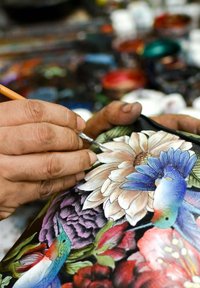Detail eines Hands, der farbenfrohe Blumenmuster auf einer dunklen Fl�äche mit einem feinen Pinsel malt. Enthält lebendige Farben und komplizierte Muster.