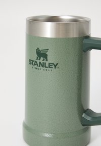 Zelený kovový hrnček s textúrovaným povrchom, nehrdzavejúci okraj a pevným držadlom. Obsahuje čierne logo s nápisom "STANLEY SINCE 1913."