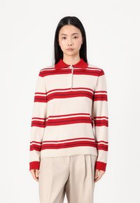 Long-sleeve polo shirt in beige with red stripes, featuring a red collar and three-button placket, made from soft knit material.