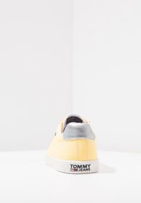Yellow canvas sneaker with a silver heel accent and white rubber sole. Features logo detailing at the back. Simple, rounded shape.