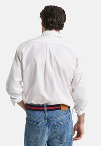 White button-up shirt with long sleeves, relaxed fit, paired with blue denim jeans and a multicolored striped belt with leather accents.