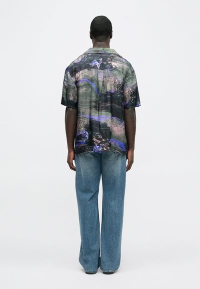 Πουκάμισο με κοντό μανίκι σε πολύχρωμο αφηρημένο σχέδιο, με άνετη εφαρμογή και καμπυλωτό τελείωμα, συνδυασμένο με ανοιχτό μπλε τζιν παντελόνι με φαρδιά πόδια.