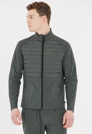 Dunkelgrüne Jacke mit durchgehendem Reißverschluss, gestepptem Oberteil und glattem unteren Stoff. Sie verfügt über einen hohen Kragen und seitliche Taschen.