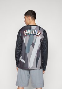 Langærmet shirt i grå camouflage med sorte ærmer. "BROOKLYN" påsyet i rød, hvid og blå på ryggen. Sammen med grå shorts.