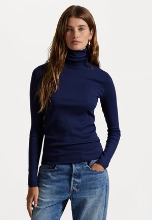 Suéter de cuello alto azul marino hecho de tela acanalada, diseño ajustado con mangas largas, combinado con jeans de mezclilla azul claro.