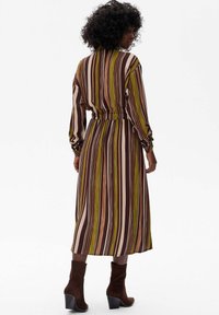 Pasiasta sukienka z długim rękawem i elastycznym pasem, w kolorach takich jak brąz, zieleń i krem. Nosi się ją z brązowymi botkami na obcasie.