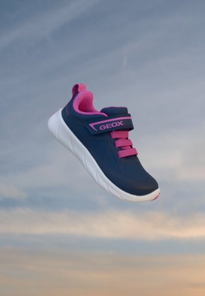Baskets Geox bleu marine et rose avec une semelle blanche flottant sur un fond de ciel doux et nuageux.