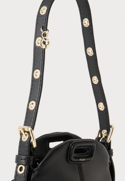 Sac à main en cuir noir avec une large bandoulière ornée d'œillets dorés et un petit pendentif doré en forme de cœur.