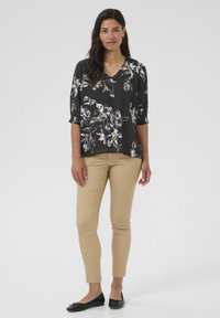Blusa nera floreale con maniche 3/4, scollatura a V e polsini elasticizzati, abbinata a pantaloni slim-fit beige e ballerine nere.