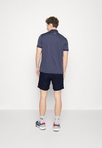 Polo à rayures marines avec manches courtes, design avec col, associé à un short sombre et des chaussures de sport. Tissu texturé et marquage minimal.