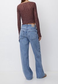 Brun, tekstureret langærmet top med en cropped kant, parret med lyseblå, løst siddende denimjeans med baglommer.