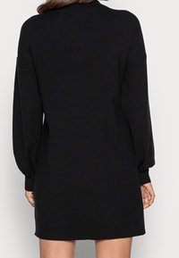 Svart stickad klänning med lång ballongärmar och lös passform. Slät textur med rund halsringning och längd som når midjan.