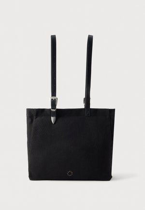 Sac cabas en toile noire avec deux longues anses en cuir, dont l’une est munie d’une boucle réglable et d’un embout argenté, sur un fond uni.