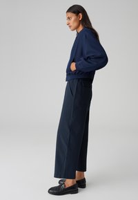 Sweatshirt court en bleu marine avec ourlet côtelé, poches latérales et coupe décontractée, associé à un pantalon large bleu marine avec poches latérales et texture lisse.