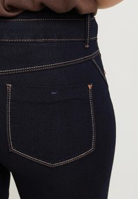 Mörk denimjeans med hög midja, med kopparstickningar, en bakficka och en slät yta.