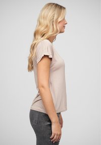 Chemise beige à manches courtes avec des poignets froncés, design ajusté et texture douce, associée à un jean gris taille haute. Composition en vue de côté.