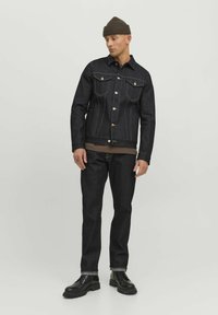 Veste en denim foncé avec deux poches poitrine, des coutures contrastantes et des boutons en cuivre. Associée à un pantalon en denim foncé et des bottes noires à lacets.