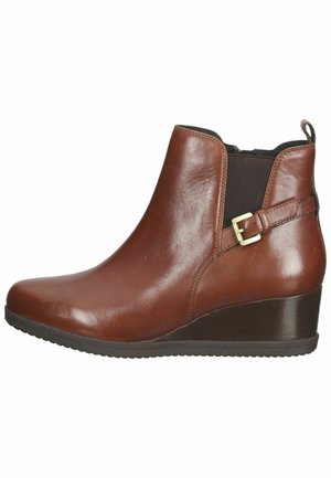 Bottine en cuir marron avec talon compensé, panneau élastique latéral et bride décorative à boucle sur fond blanc.