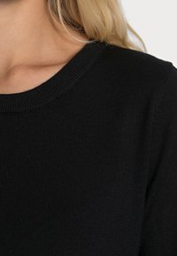 Schwarzer Strickpullover mit Rundhalsausschnitt, aus strukturiertem Gewebe. Die Nahaufnahme hebt die gerippte Nahtdetails hervor.
