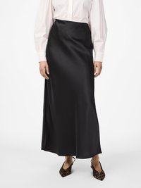 Mulher vestindo uma saia maxi preta de cetim de cintura alta, uma blusa branca de mangas longas e sapatos de salto slingback de padrão leopardo em um fundo branco.