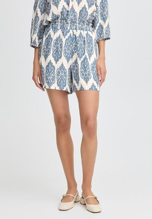 Une combinaison courte à motif bleu et blanc avec une taille ajustée, des jambes courtes et des manches amples. Le tissu présente une apparence texturée et respirante.