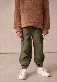 Brun fleece-pull med kvart dragkedja, parat med olivgröna cargobyxor med elastiska mudd, och vita sneakers.