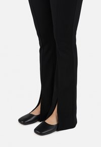 Black ribbed wide-leg pants featuring side slits, paired with flat, black leather slip-on shoes with a rounded toe design.