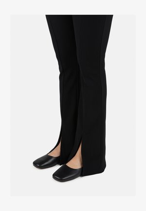 Schwarz gerippte, weite Hosen mit seitlichen Schlitzen, kombiniert mit flachen, schwarzen Leder-Mokassins im runden Zehendesign.