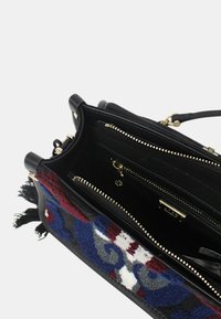 Borsa nera con tessuto testurizzato colorato su un lato, dotata di zip dorate, molteplici scomparti interni e un dettaglio frangiato.