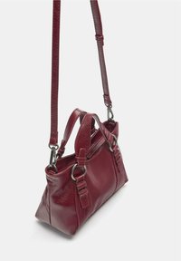 Malá červená kožená kabelka so štruktúrovaným tvarom. Má nastaviteľný ramenný popruh, dvojicu horných rukovätí a kovové ozdobné prvky.