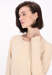 Beżowy sweter z długim rękawem, okrągłym dekoltem i ściągaczami. Miękka faktura, dopasowany fason i minimalistyczny styl.