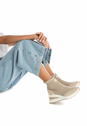Stivali ankle in maglia beige con tessuto testurizzato, punta arrotondata e suola a strisce beige e bianche, abbinati a jeans a gamba larga azzurri.