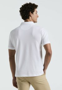Witte poloshirt met korte mouwen en een klassieke kraag, met een gladde textuur en subtiele naaddetails aan de achterkant, gecombineerd met beige broeken.