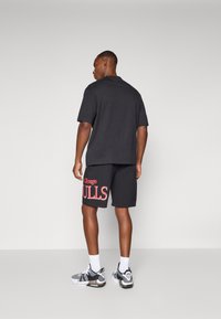 T-shirt de algodão preto, corte descontraído, combinado com calções pretos com texto vermelho "Chicago BULLS". Sapatos de desporto com pormenores em cinza e preto.