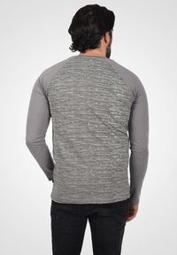 Grå langærmet skjorte med en meleret tekstur på ryggen og ensfarvede grå raglanærmer. Parret med mørke jeans.