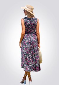 Vestido midi floral de tela azul oscuro con flores rosas y blancas, corte suelto, falda acampanada, combinado con un sombrero de paja y un bolso de mimbre.