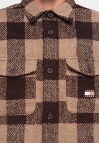 Bruine en tan geruite shirt van zachte wol, met twee borstzakken, knoopsluiting en een Tommy Jeans merklabel op de linkerzak.