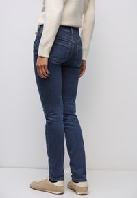 Smala blå jeans i denim med midjestorlek, femficksdesign och subtila blekningar, ihop med beige sneakers.