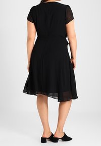 Svart klänning med korta genomskinliga ärmar, åtsittande midja och flödande kjol. Slät tyg, längd till mitten av vaden och dragkedja i ryggen. Svarta mules.