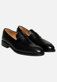 Mocassins en cuir noir avec une finition lisse, dotés d'un bout cousu et d'une sangle décorative. La semelle est plate avec un talon carré.