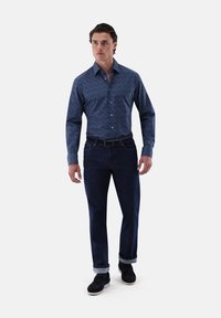 Blue patterned button-up shirt with long sleeves, paired with dark denim jeans and black shoes, featuring rolled cuffs and a belt.
