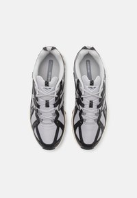 Grijze en zwarte hardloopschoenen met mesh bovenkant, gebogen ontwerp, dikke zool en opvallende veters. Voorzien van het merkembleem op de tong en aan de zijkant.