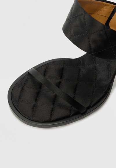 Sandal din satin matlasat negru, cu o curea lată, o curea subțire la glezna și o talpă plată cu vârf rotund. Design texturat și elegant.