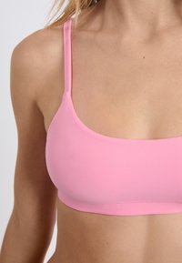Top bikini rosa con spalline sottili e un tessuto liscio e elasticizzato. Presenta un semplice scollo rotondo e un design senza cuciture per il massimo comfort.