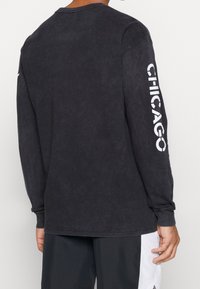 Svart långärmad t-shirt med en texturerad yta. "CHICAGO" tryckt i vitt på den högra ärmen. Klassisk passform och rundad halsdesign.