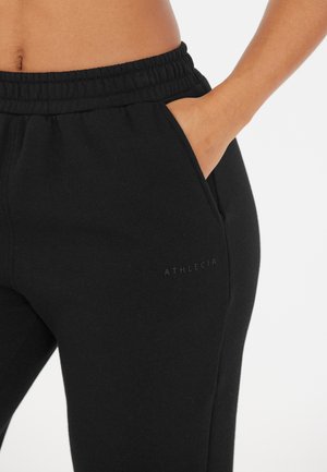 Zwarte sweatpants van een zachte stof, met een elastische tailleband en zijzakken. Subtiel "ATHLECIA" logo zichtbaar op de zijkant.