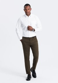 Camicia bianca a maniche lunghe con bottoni sul davanti, pantaloni verde oliva e scarpe nere stringate. Design aderente con una singola tasca sul petto.